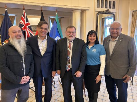A group of 5 people standing in front of flags at the launch of the First Nations: The Collection book set