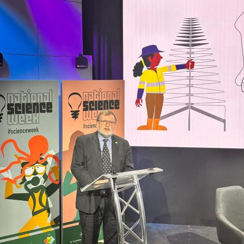 Prof Tony Haymet appears in front of a National Science Week banner, standing at a lectern. 