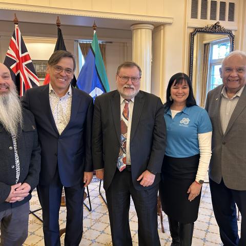 A group of 5 people standing in front of flags at the launch of the First Nations: The Collection book set