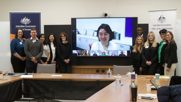 Australia's Chief Scientist, Dr Cathy Foley, standing with nine Australian Science Policy Fellows, either side of a screen with a further seven Fellows displayed.