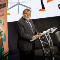 Prof Haymet stands at a lectern in front of a banner with National Science Week written on it