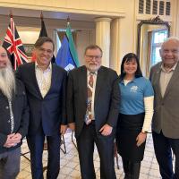 A group of 5 people standing in front of flags at the launch of the First Nations: The Collection book set